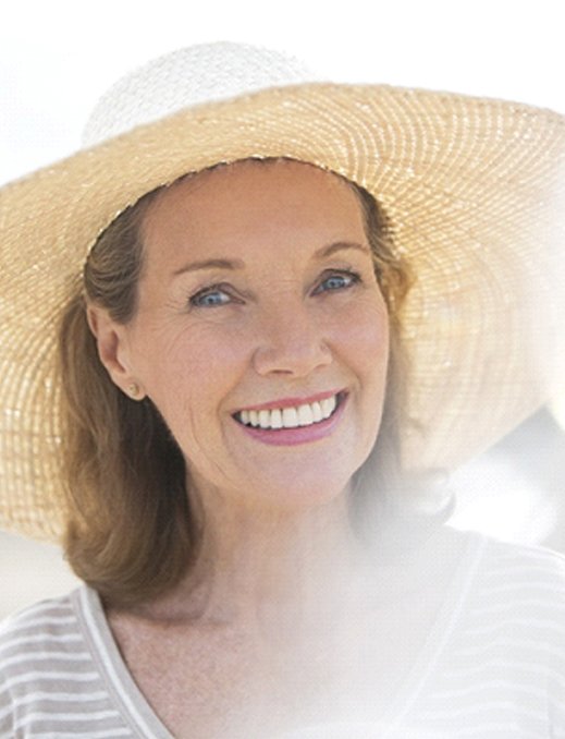 An older woman wearing a wide-brimmed hat and smiling after receiving her implant dentures in Bethel Park