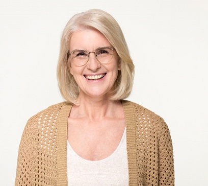 An older woman wearing a cardigan and glasses smiles after learning she qualifies for implant dentures in Bethel Park