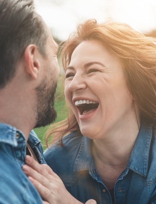 Man and woman laughing together after dental implant tooth replacement