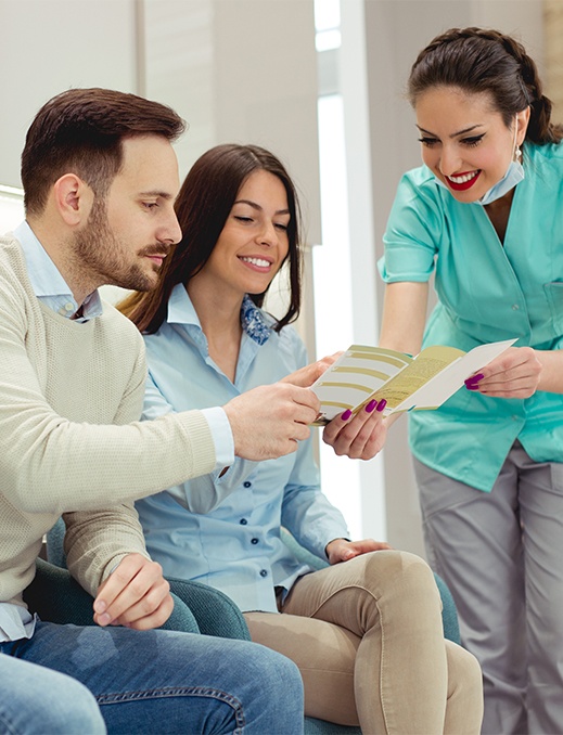 Dental team member and patients discussing dental insurance forms